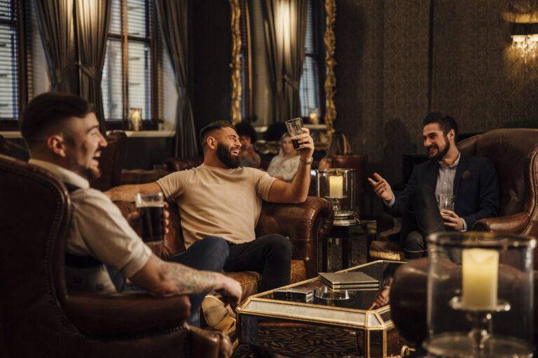 Three men are enjoying drinks in a bar lounge. They are talking and laughing while drinking pints of beer.