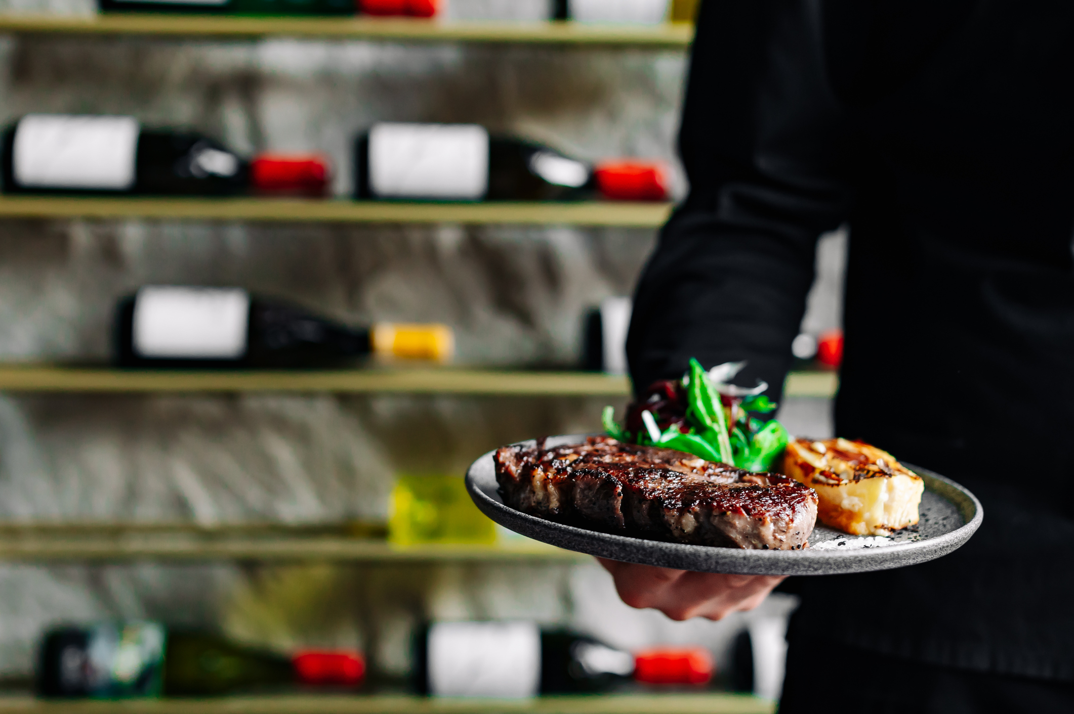 Young handsome chef in black uniform hold in his hands ready beef steak ribeye meat