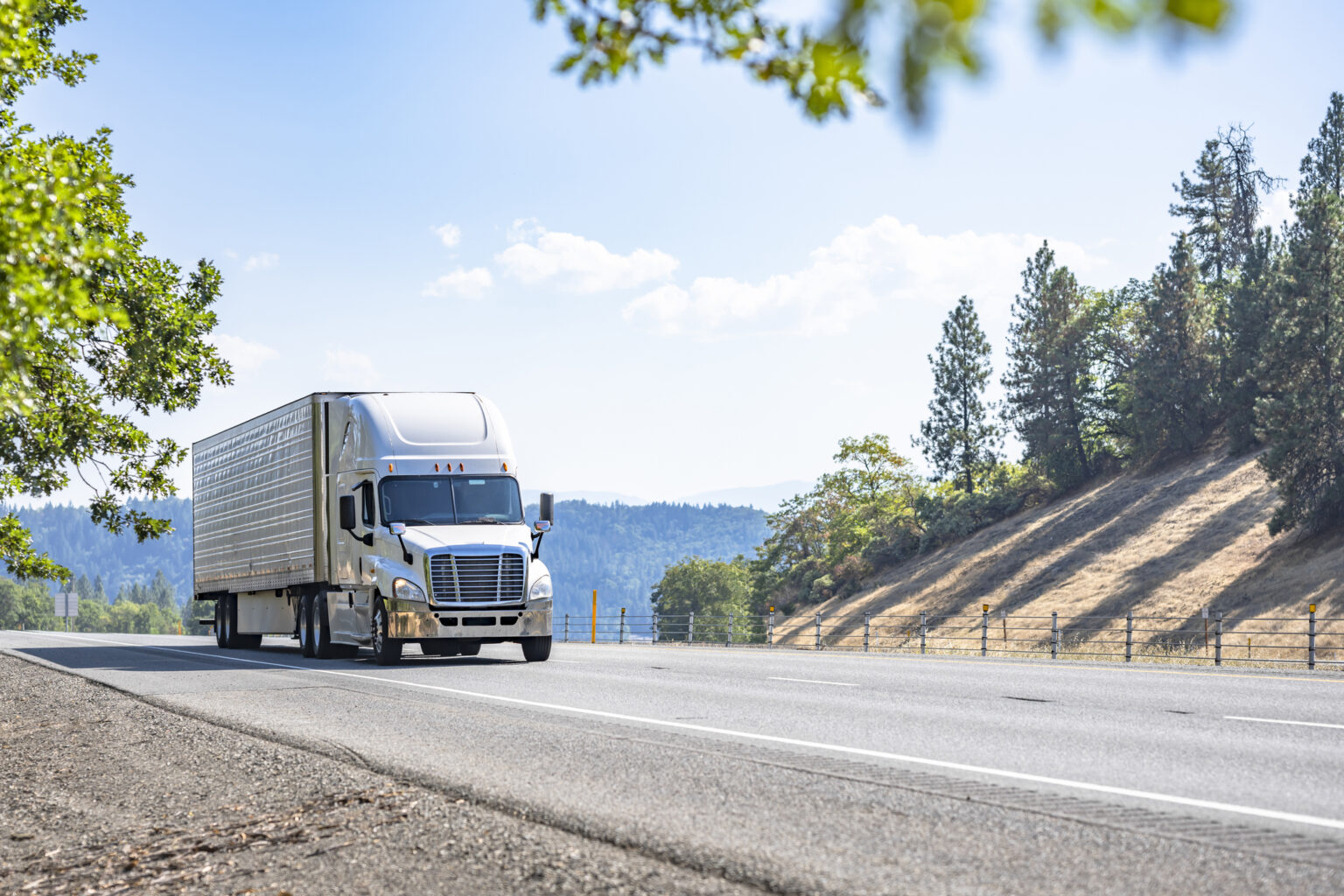 White industrial carrier big rig semi truck tractor with extended cab for truck driver rest transporting cargo in reefer semi trailer running on the one way highway road in California mountain range