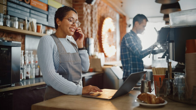 What Is a GPO? Latin American Coffee Shop Employee Accepts a Pre-Order on a Mobile Phone Call and Writes it Down on Laptop Computer in a Cozy Cafe. Restaurant Manager Browsing Internet and Talking on Smartphone.